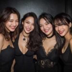 Four women smiling, wearing black dresses, ready for a night out.
